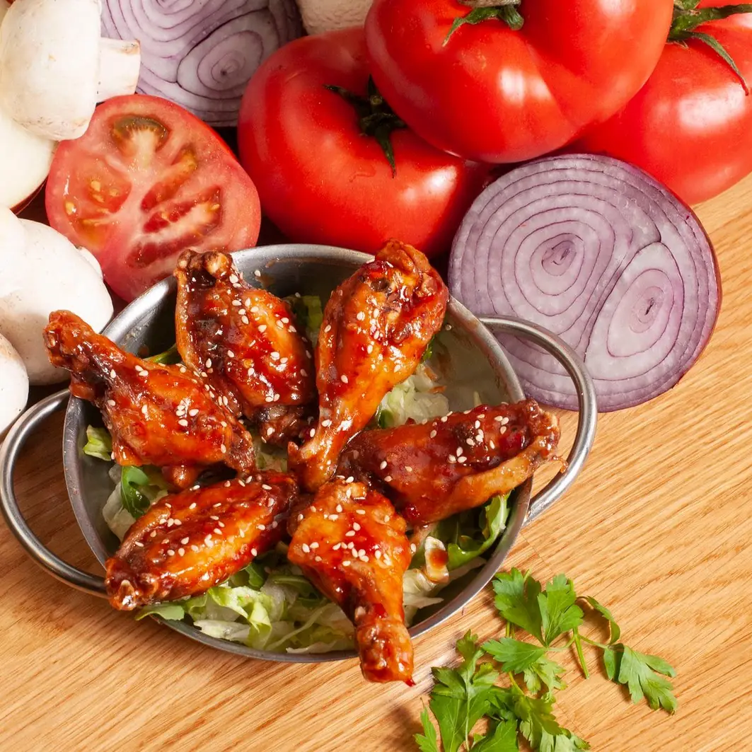 Alitas de pollo glaseadas en salsa barbacoa y sésamo, servidas en cuenco metálico sobre lechuga